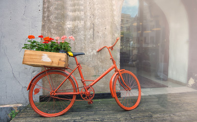 Fototapeta na wymiar An old red bike with box full of red and pink flowers stands by the wall