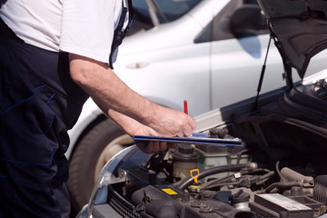 Fototapeta na wymiar Car or motor mechanic checking a car engine and writing on the clipboard