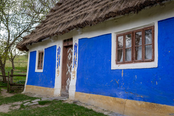 Fototapeta na wymiar National Museum Pirogovo in the outdoors near Kiev. Ancient peasant Ukrainian house with a thatched roof and cracks in the wall in the old village of national architecture.