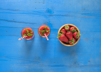 Delicious homemade strawberry smoothie on rustic blue wooden background, top view