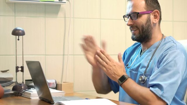 Happy male doctor finishing working on laptop and stretching arms in office
