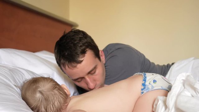 The father kisses the son who sleeps in the bed. The baby is less than two years old.