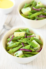 Green bean, potato and red onion salad with parsley, hollandaise sauce in the back, photographed with natural light (Selective Focus, Focus in the middle of the first salad)