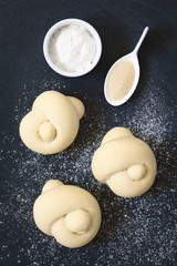 Unbaked homemade bread rolls with dried yeast and flour on the side, photographed overhead on slate with natural light (Selective Focus, Focus on the top of the rolls)