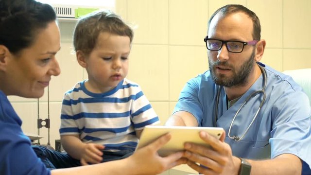 Doctor with tablet talking to mother with child about test results in office
