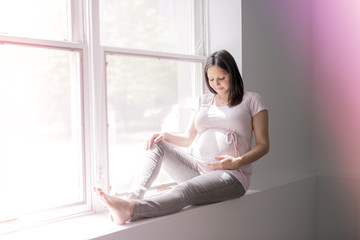 Young beautiful pregnant woman sitting on windowsill at home