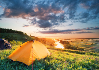 Orange tent on a hill above the river