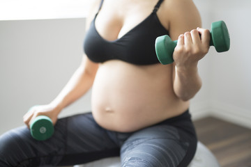 Fototapeta premium Pregnant woman training with dumbbells to stay active