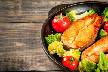 Healthy eating, diet. Baked grilled trout (salmon) with vegetable garnish - broccoli, tomatoes. In a portioned frying pan, on a wooden table. Close view copy space