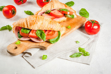 Light and hearty spring breakfast. Croissant with ham, cheese, fresh tomatoes and basil. On a white stone table, with the ingredients. Copy space