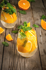 Summer refreshing orange drink. Detox, diet, infused. Variations on lemonade. Mineral water with pieces of fresh orange and mint. On a rustic wooden table. Vertical, copy space