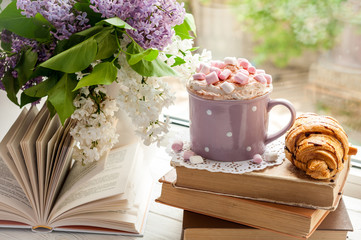 Coffee cup with marshmallow, open book, glasses, croissant and flowers bouquet on window sill. Breakfast, reading and education concept