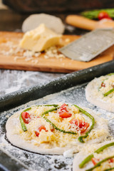 Cooking process of making mini pizza - small and personal, with cheese, tomatoes and asparagus.