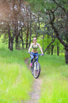 A young woman is riding a bicycle on a forest trail. Slender girl rides a bicycle, active rest.