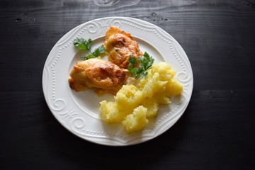 Chicken breast baked with cheese on a white plate, wooden board, close up view