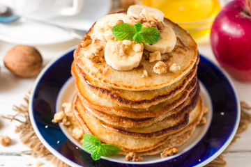 Pancakes with banana, honey, walnuts and mint on plate.