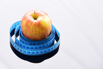 Tape for measuring wraps around red apple on grey surface