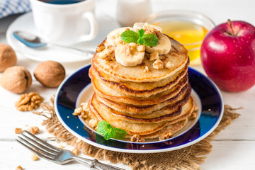Pancakes with banana, honey, walnuts and mint on plate.