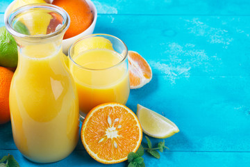 Citrus juices in jar and glass with oranges on blue wooden background