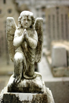 an old ivory statue of an angel kneeling to pray in a cemetry