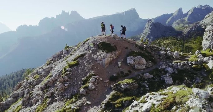 Aerial flight above people hiking along trail path in sunny day. Group of friends summer adventure journey in mountain nature outdoors. Travel exploring Alps, Dolomites, Italy. 4k drone forward video
