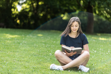 Mädchen sitzt wie in einer Gedankenblase auf Wiese und liest ein Buch