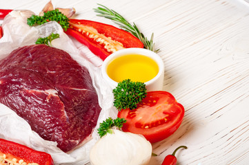 Beef meat with herbs and spices. Raw beef fillet preparation with oil, rosemary, garlic and fresh seasoning on white paper, close up. Copy space