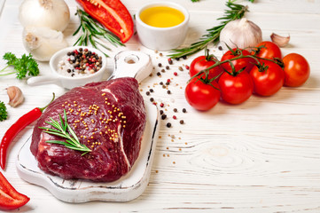 Raw meat with herbs, spices and seasoning on white wooden background, ingredients for cooking. Beef meat on cutting board, copy space