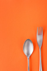 Fork and spoon on orange background, sparse composition with copy space