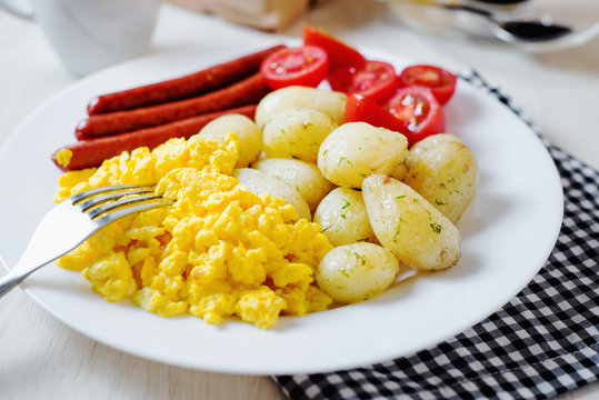 Traditional American breakfast, hotel or restaurant, boiled potato with dill, smoked sausage, omelette from chicken eggs, fresh cherry tomato, white toast, milk and black coffee on a light background