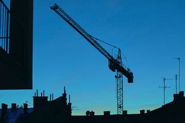 Silhouette of a building with crane on evening sky background