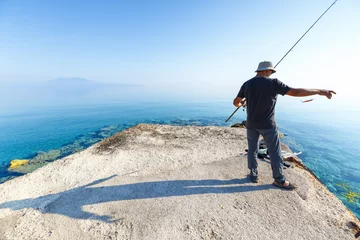 Fotobehang Side view of young man fisherman standing on pier with rod. Seashore of Ionian sea, Zante - Zakinthos island, Greece. Fishing background. Sunrise morning scenery. © Feel good studio