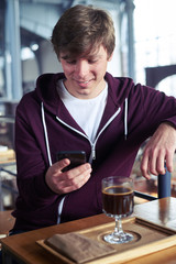 Delightful male surfing in mobile phone sitting over cup of coffee