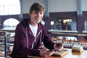 Man with beautiful smile surfing in mobile phone sitting over cup of coffee