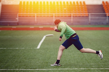 Guy with the team is throwing, throwing and catching with flying disk at the sports stadium. Concept of the game is active and mobile in summer. Sunny highlight.