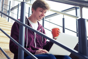 Pleased male holding cup of coffee and chatting in laptop