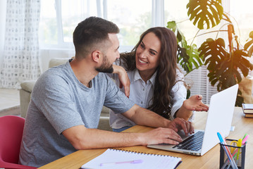 Good-looking couple smiling to each other while surfing in laptop