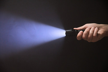 Male hand holding a led flashlight with blue beam on a black background, leaving the right side of...