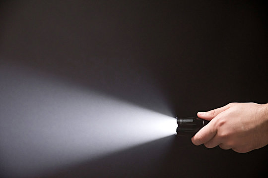 Male hand holding a led flashlight with white beam on a black background, leaving the right side of the frame