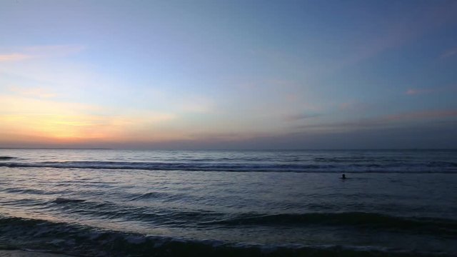 Sea scenery golden sunrise over horison. Panning left. Swimer in water. Dark waves go to sandy beach. Sound of nature. Ocean horizon beautiful background sea scene. Ocean waves sun morning sunrise