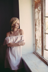 Fototapeta premium Cute blonde woman daydreaming at home, looking out window