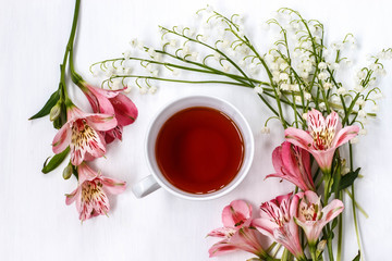 Cup of black tea with Lily of the valley and lilies on a white table