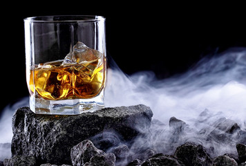 Glass of whiskey and ice.Creative photo glass of whiskey on stone with fog.Copy space.Advertising shot