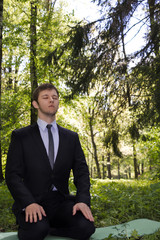Businessman meditating in nature. A man in a business suit sits in the woods in a diamond pose and meditation.