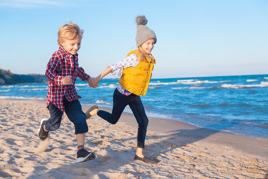 Group portrait of two funny white Caucasian children kids friends playing running on ocean sea beach at sunset, happy lifestyle childhood concept