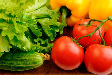 Branch of fresh red tomatoes, yellow bell pepper, green cucumbers and lettuce on a wooden cutting board
