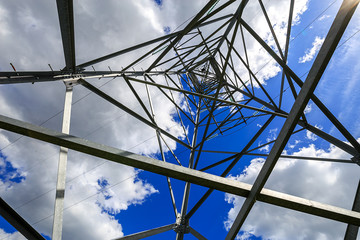 The electricity transmission pylon in daytime outdoors. Electricity tower standard overhead power line transmission tower on the background blue sky and white cloud. 