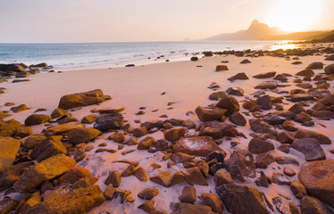 Romantic atmosphere in peaceful Sunset at Bai nhat beach Condao island-Vietnam. Taking with long exposure in the evening smooth wavy motion by Big rocks near shoreline, pink horizon with sun rays.