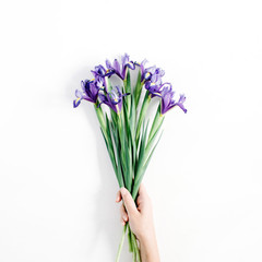 Female hand holding beautiful purple iris flowers bouquet on white background. Flat lay, top view.