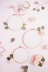 Fototapeta na wymiar Embroidery frames with beige rose flower buds and eucalyptus on pale pastel pink background. Flat lay, top view decorated concept.